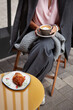 Woman sitting in outdoor cafe with cup of cappuccino coffee in her hands and croissant on table comfortably wrapped in gray plaid scarf, Because it became chilly