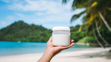Hand Holding A White Jar With A Screw Cap, Filled With Coconut Oil  In A Tropical Beach Background And Palm Trees, Clear Jar With White Cap For A Mockup