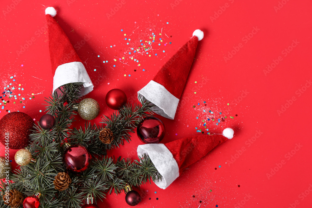 Composition with coniferous branches, Christmas decorations and Santa hats on red background