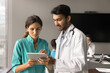 © fizkes - Couple of Indian and Latin medical colleagues consulting Internet on tablet together, using healthcare online service, application for communication, talking, discussing appointment schedule