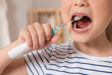 Wall Mural - Little girl brushing her teeth with electric toothbrush indoors, closeup