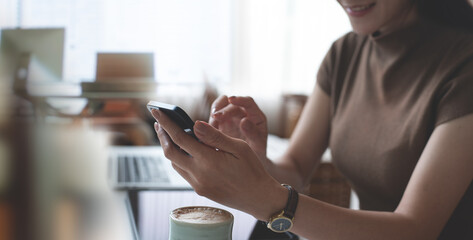 Canvas Print - Smiling casual business woman, freelancer using smartphone during online working at cafe. Happy young asian woman using mobile phone for online shopping and digital banking