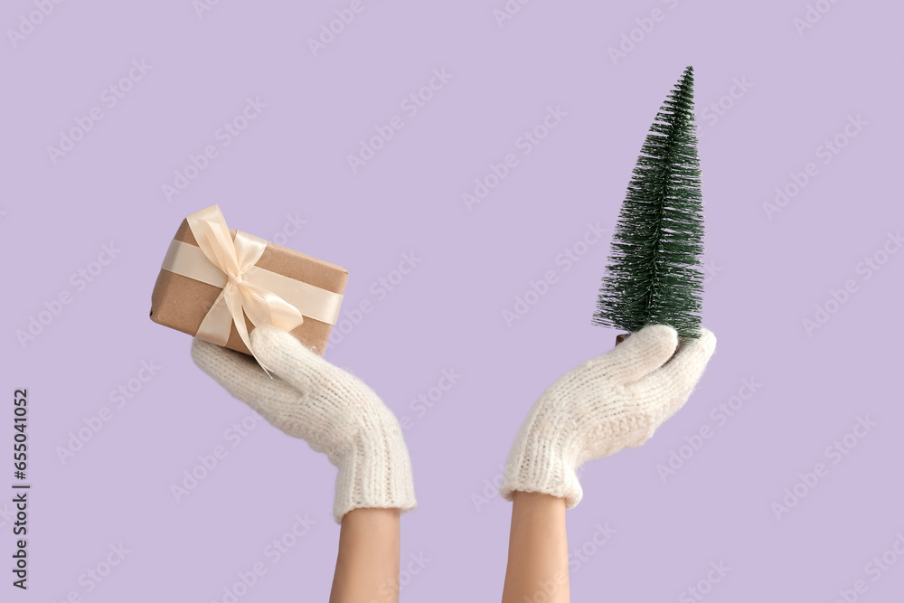 Female hands holding Christmas gift and decorative pine tree on lilac background