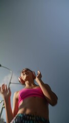 Wall Mural - A beautiful young woman in headphones and sportswear is warming up before her outdoor workout.