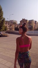 Wall Mural - A stunning, sporty woman in headphones and athletic attire is doing stretching exercises as part of her pre-workout routine on the street.