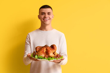 Wall Mural - Young man with tasty turkey on yellow background. Thanksgiving Day celebration