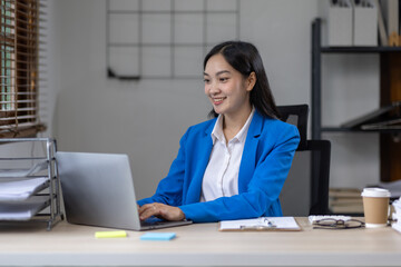 Asian busines or an accountant woman are analyzing data charts, graphs, and a dashboard on a laptop screen in order to prepare a statistical report and discuss financial data in an office.