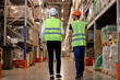 © alfa27 - rear view warehouse workers in vest and helmet walking in distribution storage area discussing, in workplace area. Concept of good management system to support working with industrial business.