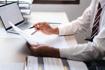 Wall Mural - Businessman reading marketing paper and checking data on laptop while analyzing strategy of startup