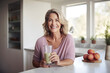 Beautiful middle-aged woman sits in the kitchen while holding a smoothie glass
