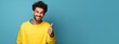 © Nanci - Portrait of cheerful young adult in yellow t-shirt showing thumbs up sign while standing isolated over blue background. Generative AI