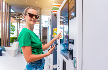 Young woman paying for coffee at vending machine using contactless method of payment 