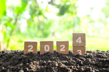 Poster - Transition change of year 2023 to 2024 in wooden blocks with growing plant at sunrise. Welcome new year 2024 and goodbye 2023 concept.