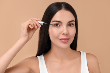 Wall Mural - Beautiful woman applying serum onto her eyelashes on beige background. Cosmetic product