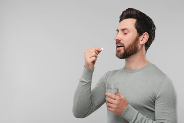 Canvas Print - Handsome man with glass of water taking pill on light grey background, space for text