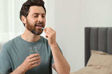 Poster - Handsome man with glass of water taking pill at home, space for text