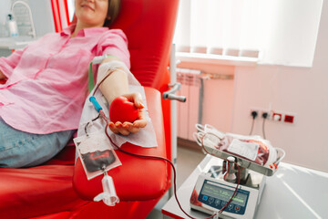 Wall Mural - Young woman making blood donation in hospital. A woman donates blood while holding a red heart. Blood donation.