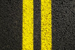 Close-up yellow dividing lines on the road with copy space. Yellow double solid line. Road markings on asphalt. Gray asphalt background with two yellow road lines. Black asphalt