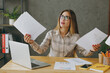 © ViDi Studio - Young dissatisfied sad employee business woman wearing shirt casual clothes glasses sit work at office desk with pc laptop hold paper account documents look overhead. Achievement career job concept.