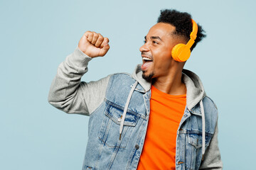 Wall Mural - Young man of African American ethnicity wear denim jacket orange t-shirt listen to music in headphones sing song in microphone isolated on plain pastel light blue cyan background . Lifestyle concept.