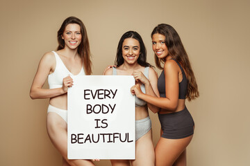 Wall Mural - Smiling millennial diverse women in underwear enjoy lifestyle, hold banner with inscription every body is beautiful