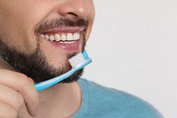 Wall Mural - Man brushing his teeth with plastic toothbrush on white background, closeup. Space for text