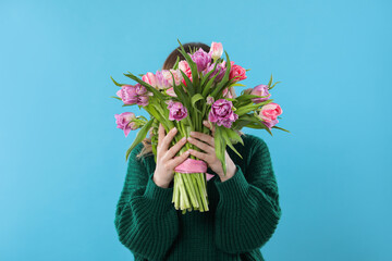 Wall Mural - Woman covering her face with bouquet of beautiful tulips on light blue background