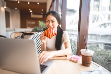 Wall Mural - Happy smile asian woman eating croissants at cafe sitting near window indoors on day