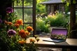 laptop open next to a garden area with blooming flowers