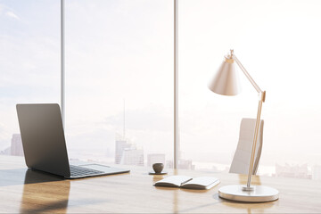 Canvas Print - Close up of modern backlit wooden desk with laptop, table lamp, coffee cup and panoramic window with city view in the background. 3D Rendering.