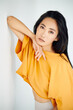 Pretty sensual asian woman in bright yellow t-shirt posing on white studio background