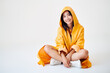 Smiling asian girl with braces dressed in bright yellow raincoat posing with hood on her head sitting on floor