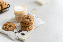 Stack Of Homemade Low-calories Banana Cookies With Oatmeal, Dark Chocolate Drops And Walnuts And A Glass Of Latte On A Light Background. Copy Space. Healthy Food. Oatmeal Biscuits. Yummy Snack