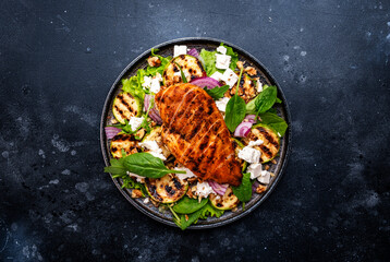 Wall Mural - Gourmet salad with zucchini and grilled chicken, feta cheese, walnut, onion and spinach, black table background, top view