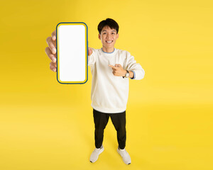 Wall Mural - full body of young Asian man wearing sweater and using phone on yellow background