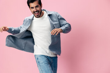 Poster - Fashion brunette man with beard happiness open mouth jumping and running with his arms spread on a pink background in a white T-shirt and jeans smile and joyful emotion on his face, copy space