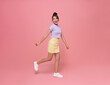 © NaMong Productions - Happy Asian teen woman smiling and walking while looking back isolated on pink background.