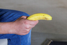 Male Hand Of Caucasian Man Holding Unpeeled Banana Between Legs