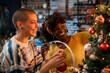 © Marko Geber - Happy young interracial lesbian couple decorating a Christmas tree during the holidays at home