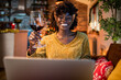 © Marko Geber - Young African American woman drinking wine while using a laptop in her home decorated for the Christmas and new year holidays