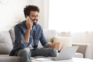 Wall Mural - Young Indian Man Talking On Cellphone While Sitting On Couch At Home