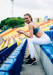 Wall Mural - Cheerful young athletic woman browsing phone in stadium