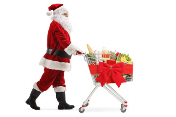 Sticker - Full length profile shot of Santa Claus walking and pushing a shopping cart with a red ribbon bow