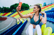 © BullRun - Braided sporty young woman capturing selfie by mobile in grandstand