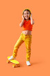 Leinwandbild Motiv Cute little girl in headphones with skateboard on orange background