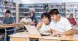 © JackF - Concentrated asian teenager female schoolgirl and her male friend sitting at library desk with laptop, doing homework with internet