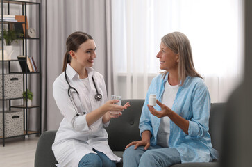 Sticker - Young healthcare worker giving glass of water to senior woman with pills indoors