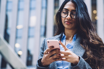 Wall Mural - Young ethnic woman in glasses with phone on street