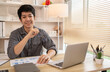© Puwasit Inyavileart - Handsome young man sits working at a desk with a laptop and office equipment, Smiling young man ready for work at the start of the week. Positive Start to a Productive Workweek.