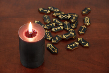 Wall Mural - Burning black witch candle and black runes on wooden table.	